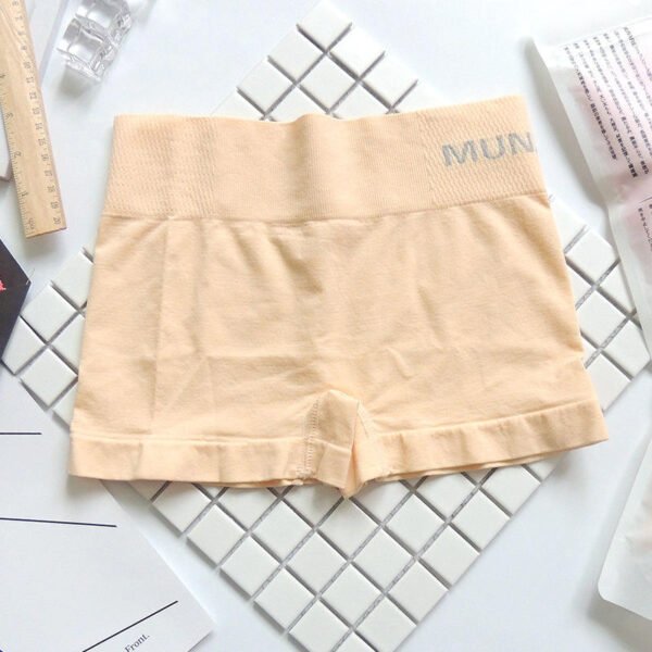 A pair of light peach Munafie Shorts displayed on a tiled surface, surrounded by a ruler and other items.